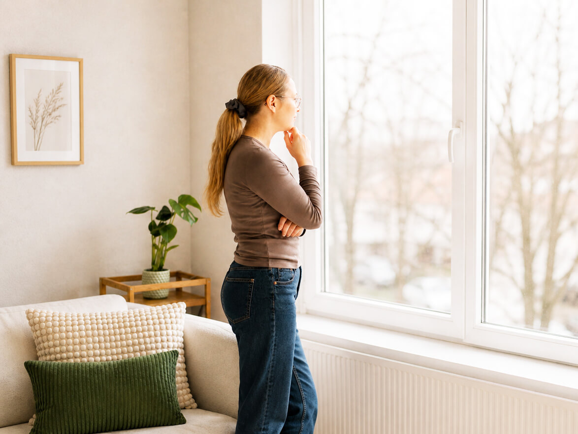 Nachdenkliche Mutter blickt am Fenster in die Ferne